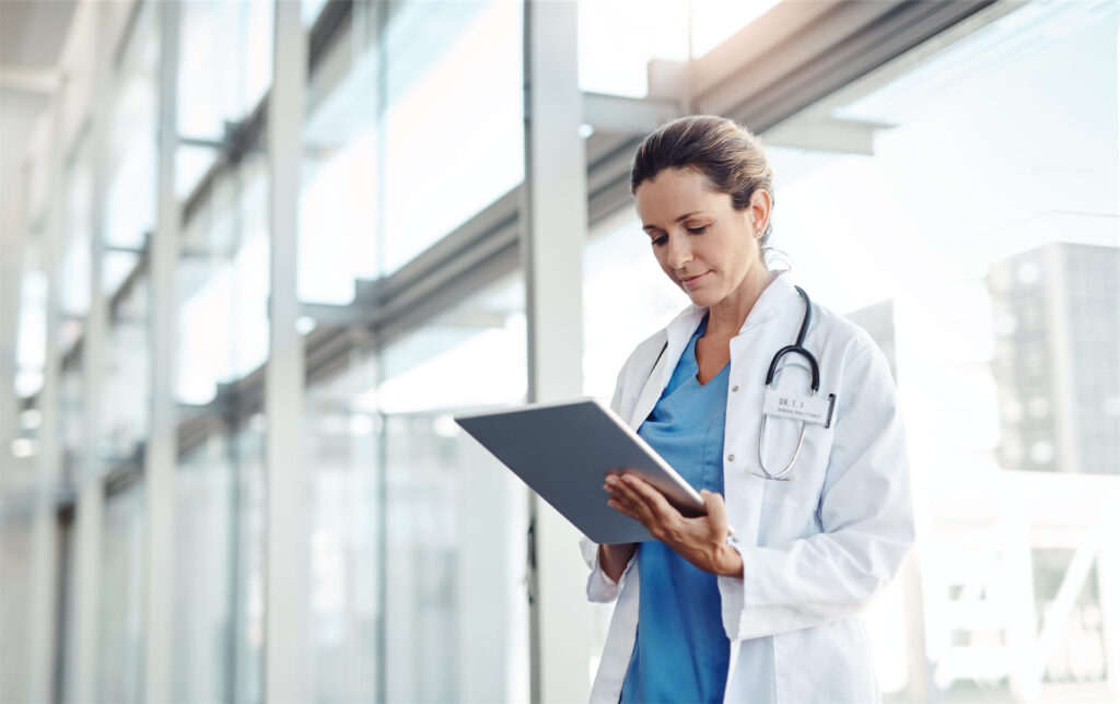 Femme médecin en train de consulter un document, debout dans les couloirs.